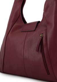 Bordeaux leren schoudertas met een soepele textuur, voorzien van een handvat bovenaan, een magnetische klepsluiting en een zijvak met rits.