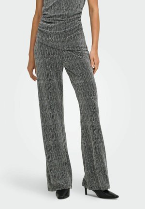 Femme portant un pantalon gris texturé taille haute à jambes larges, associé à un haut froncé assorti et des talons pointus noirs.