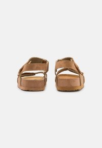 Sandalias marrones con correas entrelazadas, textura suave de ante, plantillas acolchadas, parte trasera abierta y suelas de goma para tracción.
