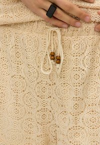Kanten haakshorts in lichtbeige, met een trekkoord met houten kralen en een textuurpatroon van circulaire ontwerpen.