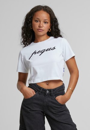 White cropped t-shirt featuring black cursive text "pequs" across the front. Paired with dark denim pants, showcasing a casual style.