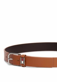 Cinturón de cuero marrón con un acabado suave, que presenta una hebilla de metal plateado y un acento de logo rectangular que muestra colores rojo, blanco y azul.