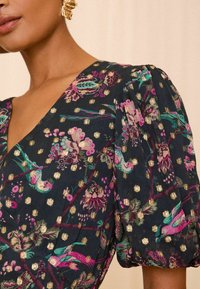 Blommönstrad klänning med puffärmar, djup V-ringning, mörk bakgrund med gulddotsdetaljer och flerfärgad fågel- och blommönster.