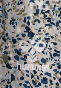 Gelegenheid stof met blauwe, groene en witte bloemenmotieven. Bevat een witte reliëflogo met de tekst "hummel" op een beige achtergrond.