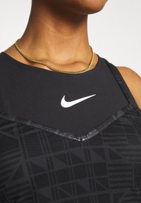 Närbild av en person som bär en svart Nike sporttopp med en vit swoosh-logotyp och ett guldhalsband.