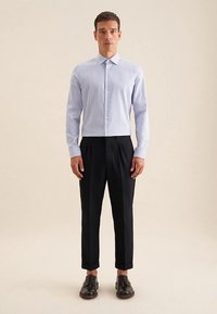 Camicia a maniche lunghe a righe azzurro chiaro e bianco, abbottonata, con colletto; abbinata a pantaloni sartoriali neri e scarpe nere.