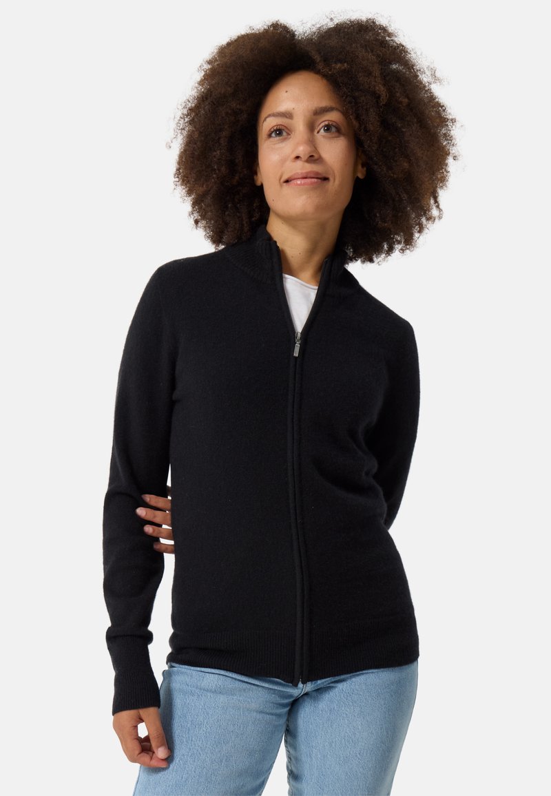 Musta vetoketjulla varustettu pitkä neuletakki, joka on valmistettu pehmeästä kankaasta ja jossa on korkea kaulus sekä ribbauskantit. Yhdistetty vaaleansiinisiin farkkuihin.