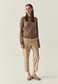 Pull en mélange de laine marron avec col rond, associé à un pantalon beige fuselé et des baskets vert olive. Texture lisse et coupe décontractée.