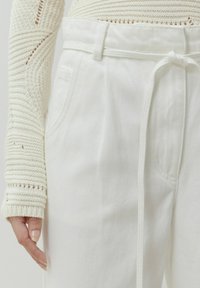 Witte katoenen broek met een trekkoord in de taille, voorzien van zijzakken en een soepele textuur. Gebreide witte sweater mouw getoond.