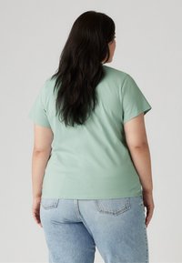 Mint green, short-sleeve t-shirt made of soft fabric. The back features a rounded hem and slight side vent accents. Worn with light blue jeans.