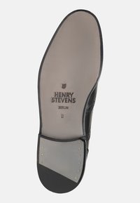 Suola di scarpa in pelle nera con superfice grigia liscia, logo in rilievo "HENRY STEVENS BERLIN" e piccoli chiodi decorativi dorati sul bordo.