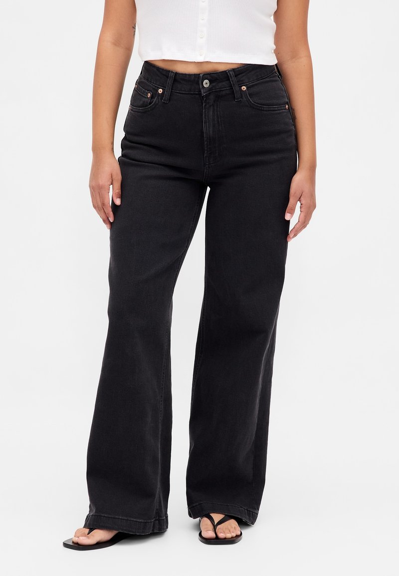 Crne traperice širokih nogavica s visokim strukom, izrađene od trapera. Imaju prednje džepove, zatvaranje na gumb i čist završetak. Tkanina s teksturom.