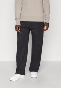 Μαύρο παντελόνι φόρμας με άνετη εφαρμογή, κατασκευασμένο από μαλακό ύφασμα. Διαθέτει πλαϊνές τσέπες και ελαστική μέση με κορδόνι. Συνδυάζεται με λευκά αθλητικά παπούτσια.