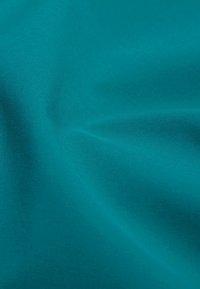 Tessuto teal con una superficie liscia e leggermente texture. Il materiale appare leggero, scende dolcemente con pieghe e crepe delicate.