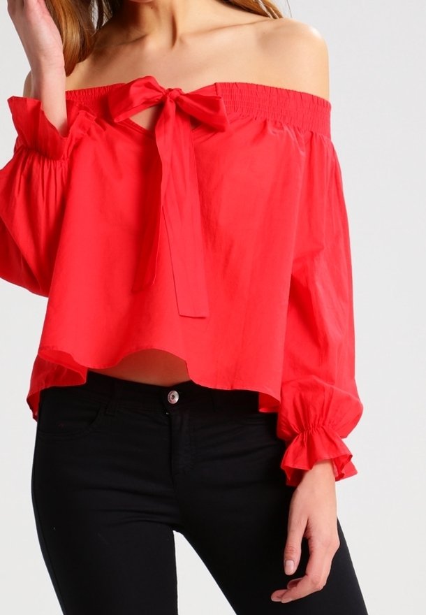 Blouse rouge à épaules dénudées avec un nœud au niveau du col, taille smockée et longues manches à volants. Le tissu semble léger et lisse.