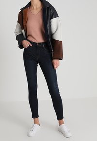 Kožená bunda s barevnými bloky v hnědé, bílé a námořnické; těsné světle růžové tričko; tmavé džíny s vysokým pasem; bílé tenisky.