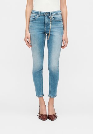 Slim fit ανοιχτό μπλε τζιν, φορεμένα με μπορντό μυτερά τακούνια και αξεσουάρ αλυσίδας με πέρλες προσαρτημένο στον μπροστινό θηλιά της ζώνης.