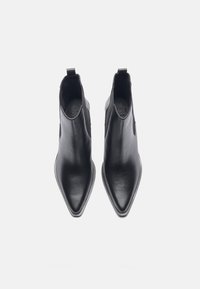 Botines de cuero negros hasta el tobillo con puntera afilada, textura suave y paneles laterales elásticos. Incluye una lengüeta en la parte trasera para facilitar su puesta.