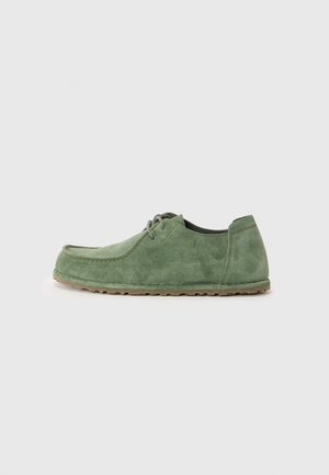 Grüne Wildlederschuhe mit runder Zehenpartie, Schnürdesign und strukturierter Oberfläche. Die Laufsohle ist hellbraun und vermittelt ein lässiges Aussehen.