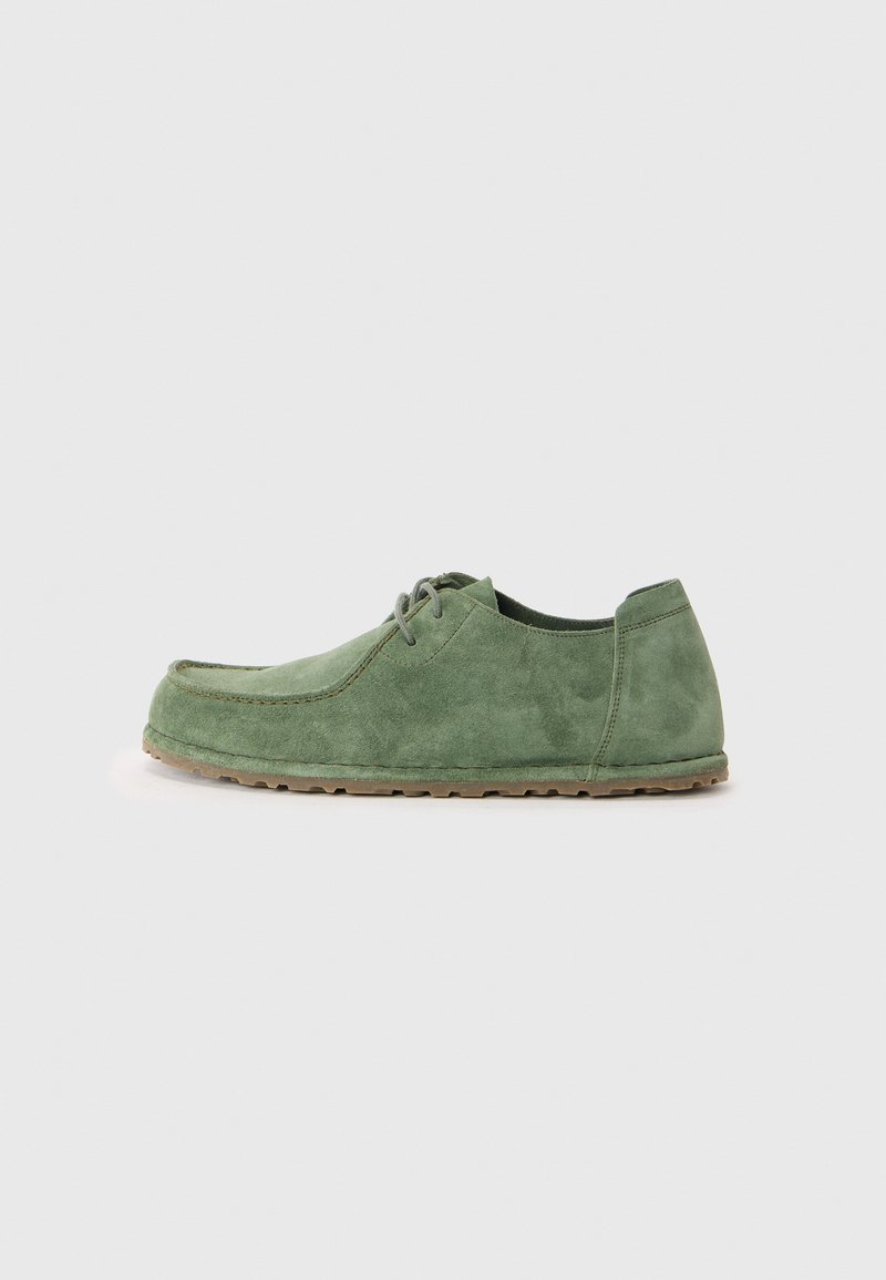 Sapatos de camurça verdes com bico arredondado, design com atacadores e uma superfície texturizada. A sola externa é castanho claro e oferece uma aparência casual.