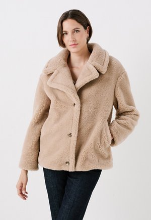 Beige nepbontjas met een brede kraag, knopen aan de voorkant en zijzakken. Heeft een gestructureerde afwerking en een relaxed fit.
