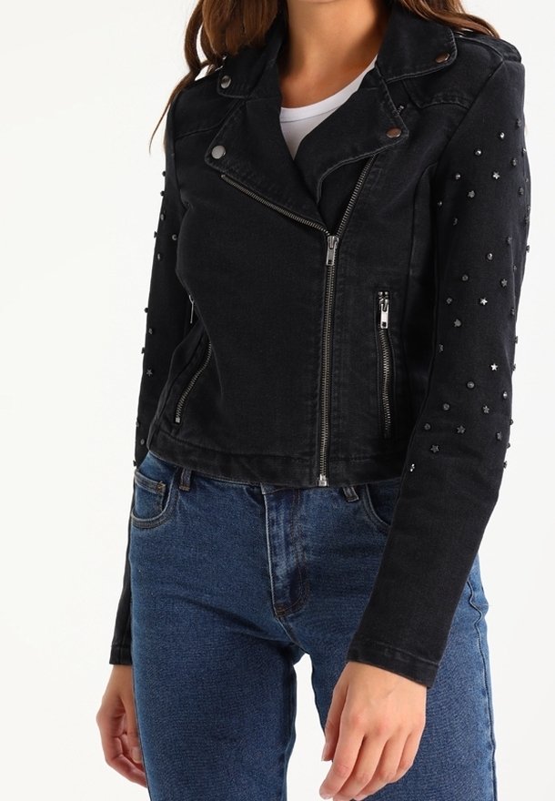 Femme portant une veste de motard noire zippée avec des embellissements en forme d’étoile et de perles sur les manches et un jean en denim bleu.