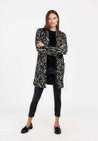 Długi kardigan z otwartym przodem w stonowanym czarno-beżowym wzorze zebry, z dwoma przednimi kieszeniami i prążkowanymi mankietami, zestawiony z czarnymi skórzanymi spodniami.