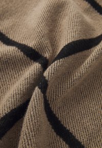 Tissu beige présentant un motif de carreaux noirs en diagonale. La texture semble douce, avec un tricot fin et un léger côtelé.