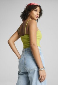 Top a maniche corte aderente di un brillante verde con un paio di jeans in denim azzurro chiaro a vita alta. Presenta spalline sottili e dettagli in argento ben visibili.