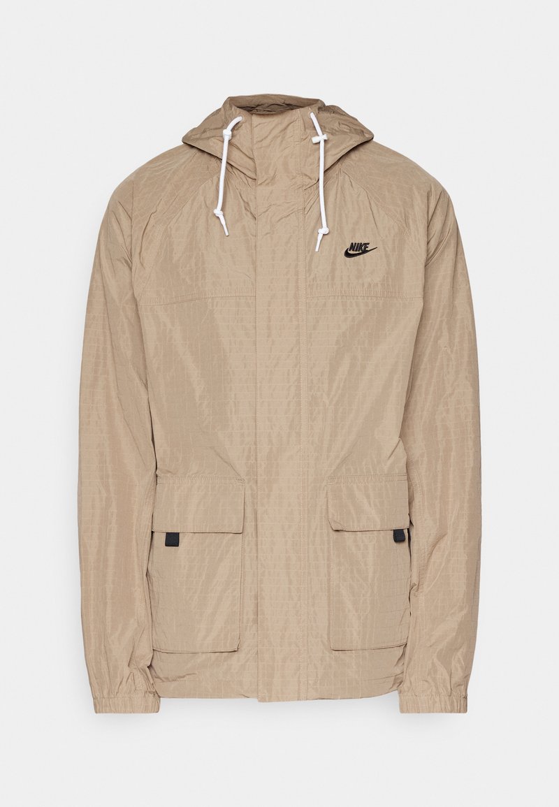 Chaqueta beige ligera con un acabado texturizado, capucha ajustable y cordones blancos; cuenta con dos bolsillos delanteros y un logo negro.