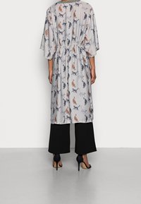 Lätt, mönstrad kappa med katter i olika färger, med en insvängd midja och vida ärmar, kombinerad med svarta, vida byxor och klackar.