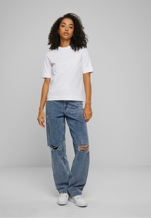 T-shirt en coton blanc à manches courtes associé à un jean bleu ample et déchiré, avec des déchirures aux genoux, et des baskets blanches.