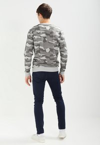Sudadera de camuflaje gris con mangas largas y cuello redondo, combinada con pantalones azul oscuro y zapatillas blancas. Tejido suave y diseño ajustado.