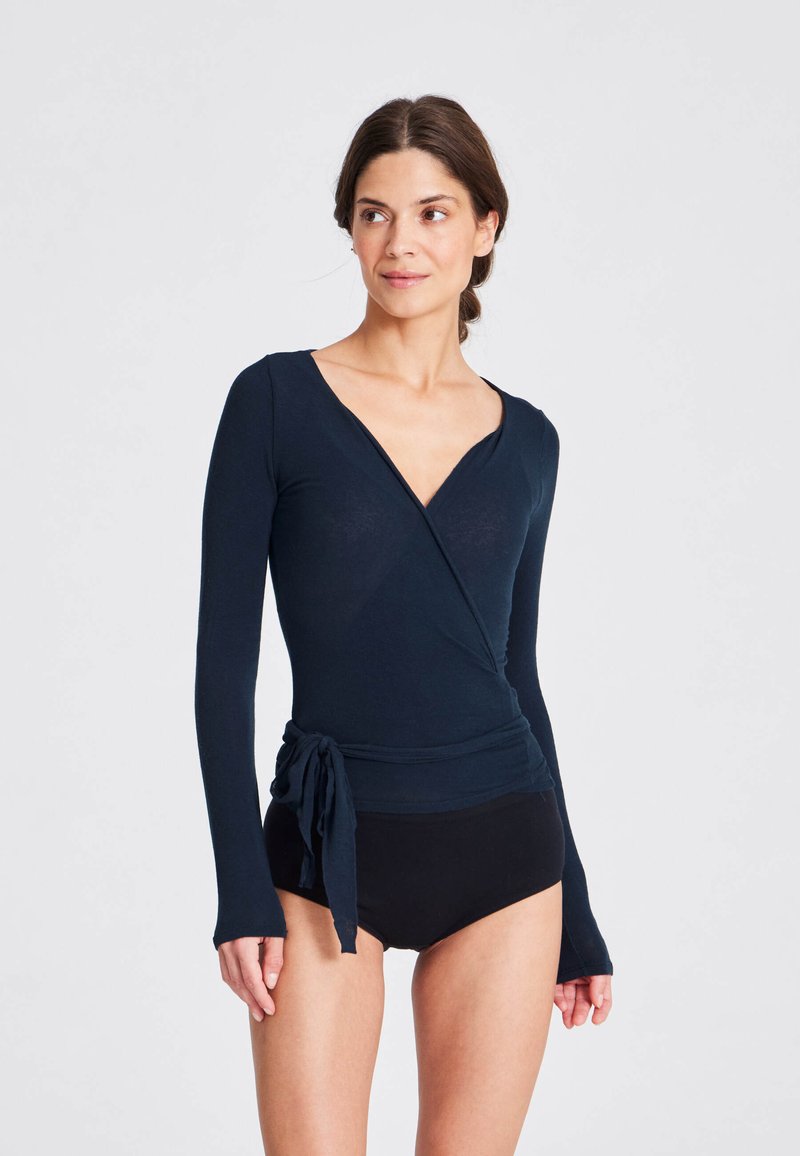 Maglietta avvolgente a maniche lunghe blu navy con scollatura a V e dettaglio in vita annodato, abbinata a pantaloni corti neri. Tessuto dalla texture liscia, design aderente.