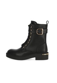 Botas de tobillo de cordones negras hechas de cuero, con herrajes en tono dorado, un acento de hebilla lateral y una suela de goma gruesa con detalle metálico.