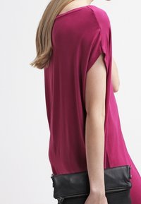 Fuchsia short-sleeve top with a relaxed fit, paired with a black clutch. The fabric appears smooth with a slight sheen.