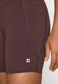 Burgundi színű sportnadrág, rugalmas anyagból készült, fehér logo részletekkel és sima varrással a letisztult megjelenés érdekében.