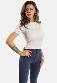 Weißes enges T-Shirt mit kurzen Ärmeln, kombiniert mit navyfarbene High-Waist-Leggings, die über einen Reißverschluss vorne und eine glatte Textur verfügen.