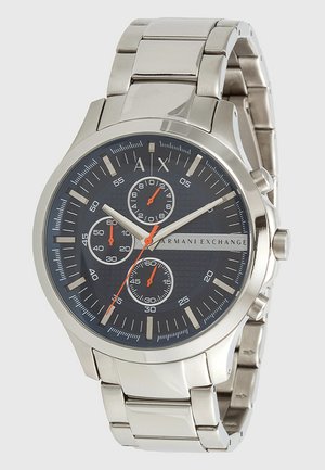 Reloj de acero inoxidable plateado con un dial texturizado en azul oscuro, tres subdiales, marcadores de horas plateados y acentos naranjas. Brazalete de metal.