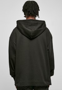 Svart oversized hettegenser med stor hette, lange ermer og ribbestrikket kant. Glatt tekstur med minimalt med detaljer.