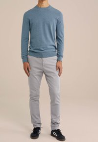 Blå stickad tröja med rund hals, kombinerad med ljusgrå slim-fit byxor och svarta sneakers med vita ränder. Slät textur och figurnära design.