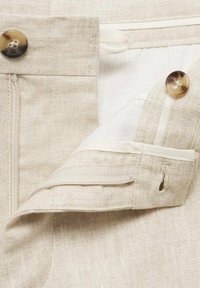 Linen trousers in light beige with a textured finish. Features include a zip fly, two buttons, and a concealed pocket for secure storage.
