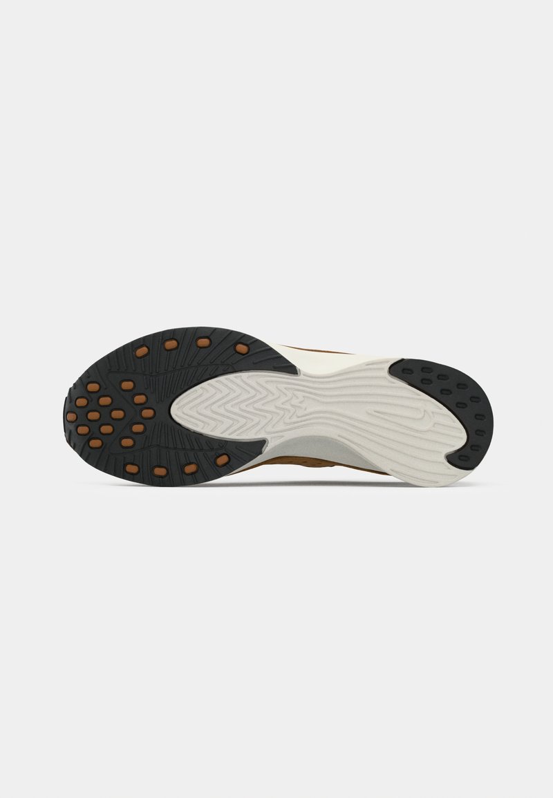 Semelle de chaussure avec une surface en caoutchouc noir texturé, des points de traction orange et une semelle intermédiaire blanche. Le design comporte des rainures pour la flexibilité.