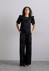 Juodas apranga, kurią sudaro prigludęs marškinėliai su pūstomis rankovėmis ir gėlių paillettes dekoracijomis, derinama su plačiakelnėmis kelnėmis, abi iš glotnaus audinio.