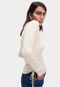 Crème lange mouw top met een aansluitend ontwerp, koord aan de taille en een zachte textuur, gecombineerd met blauwe denim jeans.