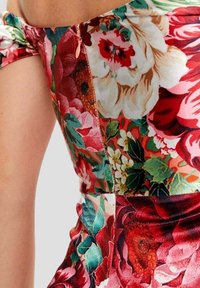 Robe fleurie aux couleurs vives incluant le rouge, le rose et le vert. Fabriquée en tissu lisse, avec une coupe ajustée et un détail de fermeture éclair visible.