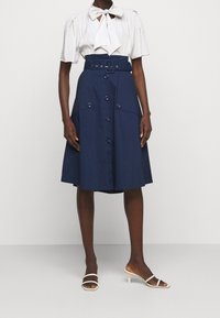 Námořnická A-line sukně s opaskem, knoflíkovými detaily a bočními kapsami. V kombinaci s bílou blůzou s mašlí na výstřihu a krátkými rukávy.