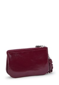 Portafoglio in pelle bordeaux con finitura lucida. Presenta una chiusura con zip e una catena decorativa con un ciondolo stilizzato. Design compatto e rettangolare.