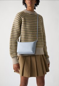 Borsa a tracolla in pelle azzurra con un design minimalista, texture liscia e una sola tracolla, abbinata a un maglione a righe e a una gonna plissettata.