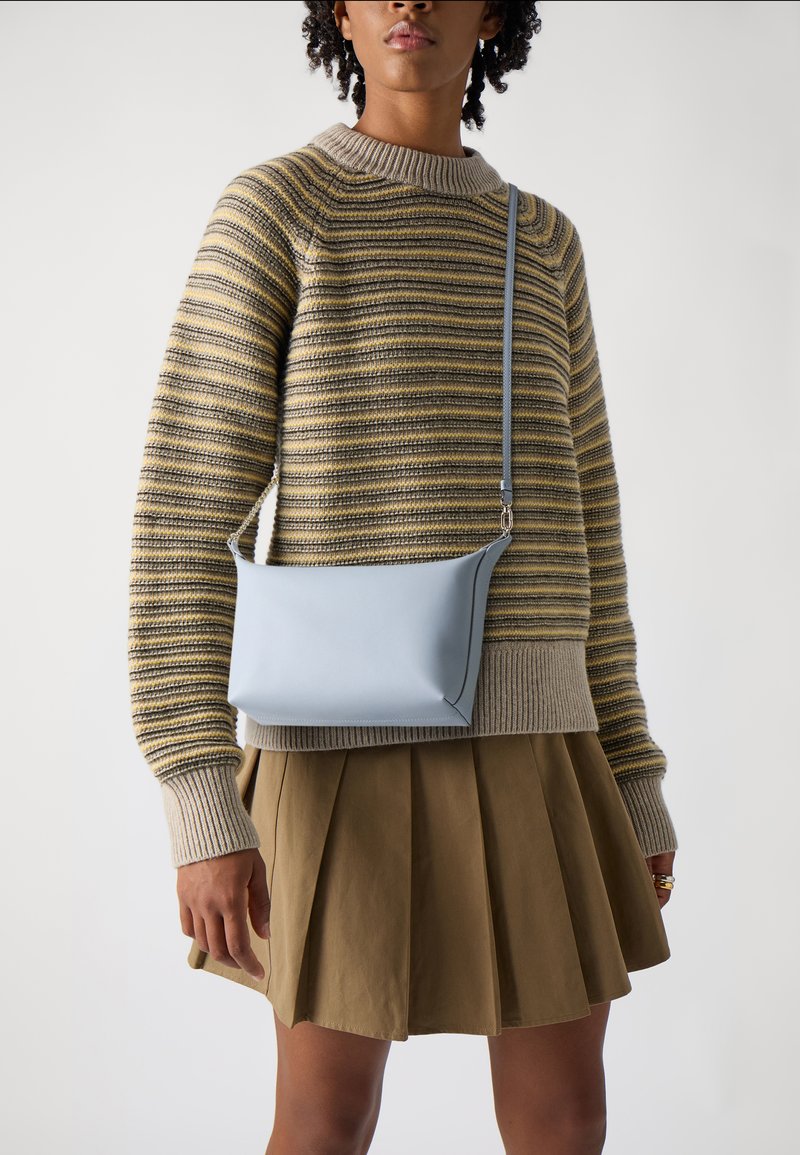 Borsa a tracolla in pelle azzurra con un design minimalista, texture liscia e una sola tracolla, abbinata a un maglione a righe e a una gonna plissettata.